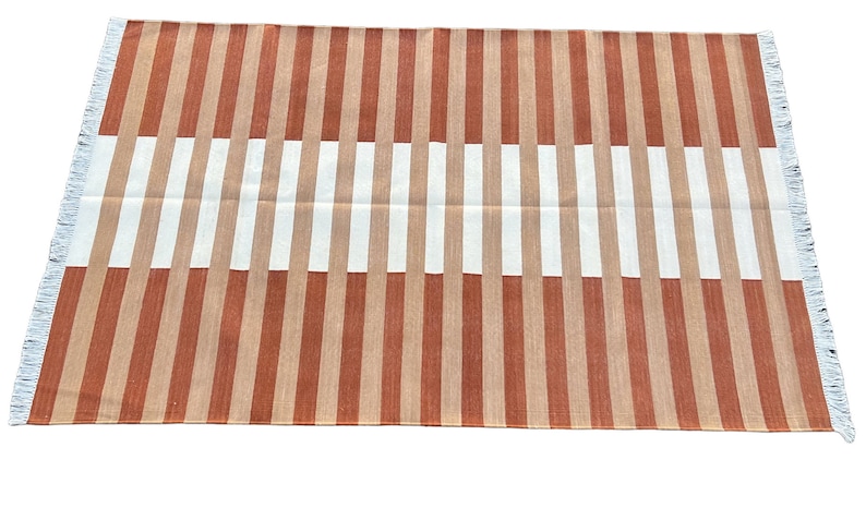 K&ouml;nnte beinhalten: Ein gestreifter Teppich mit abwechselnden B&auml;ndern in Orange und Wei&szlig;. Der Teppich hat einen Fransenrand.