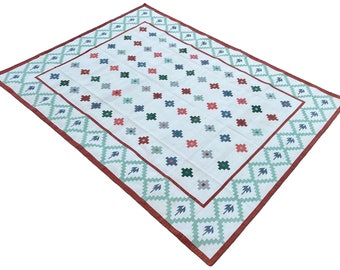 May include: A white rug with a geometric pattern in shades of red, green, and blue. The rug has a border with a diamond pattern.