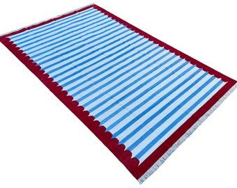 Op de afbeelding: Een blauw-wit gestreept tapijt met een rode gegolfde rand en franjes.