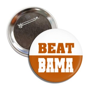 May include: A white and orange button with the text "BEAT BAMA" in white letters on an orange background.