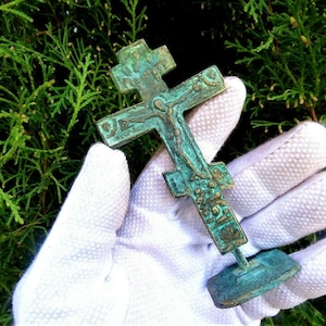 May include: A small, green, bronze cross with a figure of Jesus Christ on it. The cross is on a small, green, bronze base.