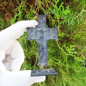 May include: A small, black metal cross with intricate details. The cross is on a stand and has a bird design in the center.