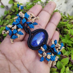May include: A blue and gold macrame necklace with a large blue gemstone pendant.