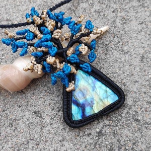 May include: A black cord necklace with a blue and gold macrame tree pendant featuring a triangular iridescent gemstone.