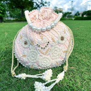 Puede incluir: Un bolso de cord&oacute;n rosa con cuentas, ribete de perlas y borla. El bolso est&aacute; decorado con bordados florales y lentejuelas.