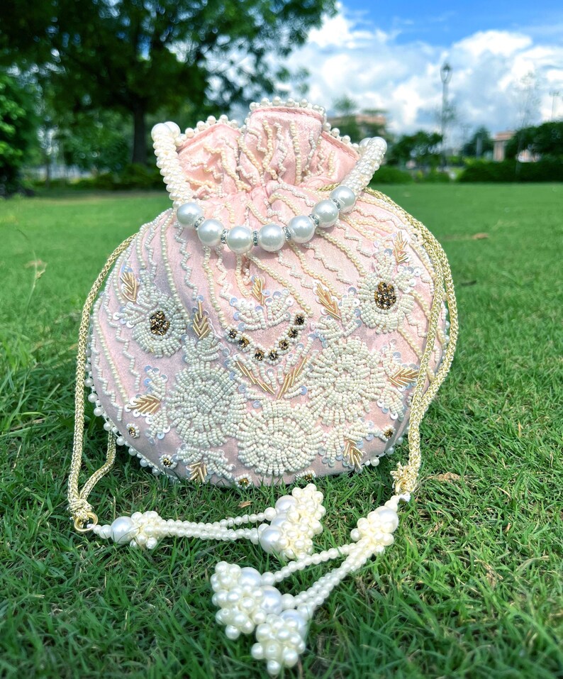 Puede incluir: Un bolso de cord&oacute;n rosa con cuentas, ribete de perlas y borla. El bolso est&aacute; decorado con bordados florales y lentejuelas.