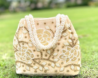 May include: A cream velvet handbag with a floral design embroidered with gold and white beads. The bag has a pearl strap.
