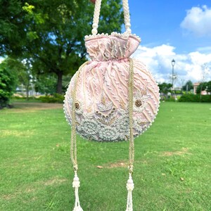 Puede incluir: Un bolso de mano de color rosa y blanco con cuentas, con un asa de perlas y detalles de borlas.