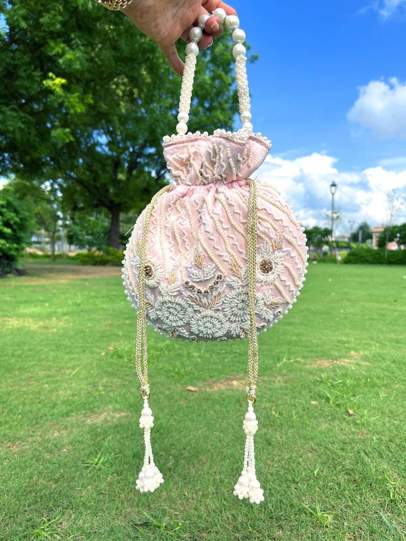Puede incluir: Un bolso de mano de color rosa y blanco con cuentas, con un asa de perlas y detalles de borlas.
