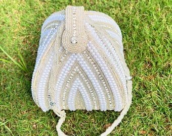 May include: A white beaded clutch bag with a geometric design. The bag has a short handle and is made of small white pearls and rhinestones.