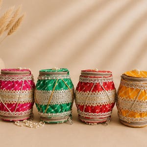 May include: Four cylindrical fabric bags in hot pink, emerald green, red, and yellow, each featuring a white checkered pattern, metallic silver lace trim, and a top zipper closure with a small pearl bead accent on the zipper pull.