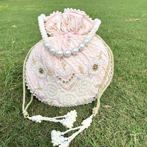 Puede incluir: Un bolso de cord&oacute;n rosa con cuentas, con una correa de cadena dorada y un borla. El bolso est&aacute; decorado con bordados blancos y dorados.