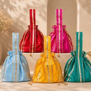 May include: A collection of five drawstring pouches in red, magenta, light blue, yellow, and teal. Each pouch features a vertical handle with gold metallic trim, a gathered top closure with matching gold drawstrings, and decorative gold piping.