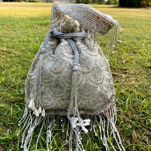 Puede incluir: Una bolsa de cord&oacute;n de cuentas plateadas con un borla blanca. La bolsa est&aacute; decorada con un patr&oacute;n de peque&ntilde;as cuentas redondas.