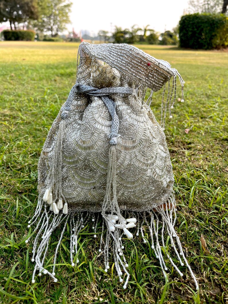 Puede incluir: Una bolsa de cord&oacute;n de cuentas plateadas con un borla blanca. La bolsa est&aacute; decorada con un patr&oacute;n de peque&ntilde;as cuentas redondas.