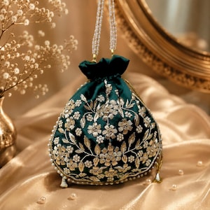 Pode incluir: Uma bolsa tipo saco verde-escura com fecho de cordão, decorada com bordados florais metálicos dourados e pequenos detalhes de pérolas brancas. A bolsa possui um topo franzido e uma alça longa feita de vários fios de pequenas contas brancas.