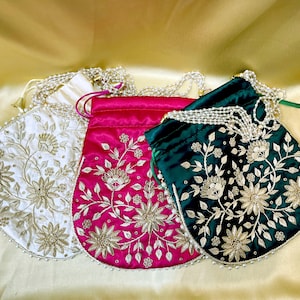 May include: Three embroidered drawstring bags in white, fuchsia, and emerald green. Each bag features floral embroidery in gold thread and a beaded drawstring closure. The bags are made of a satin-like material and are suitable for carrying small items.