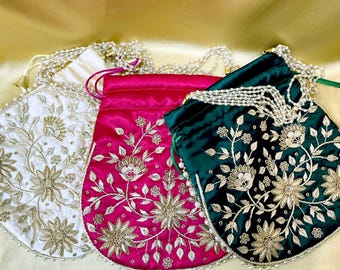 Puede incluir: Tres bolsas bordadas con cordón en blanco, fucsia y verde esmeralda. Cada bolsa presenta bordados florales en hilo dorado y un cierre de cordón con cuentas. Las bolsas están hechas de un material similar al satén y son adecuadas para transportar objetos pequeños.