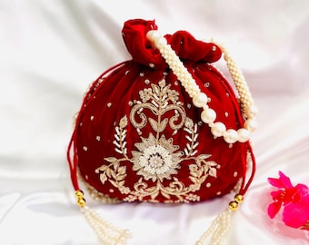 Op de afbeelding: Een rode fluwelen tas met trekkoord, versierd met gouden en witte bloemenborduurwerk. De tas heeft een parelmoeren handvat en kwastjes. Het ontwerp is elegant en geschikt voor speciale gelegenheden.