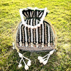 May include: A green velvet drawstring bag with gold and white embroidery and a pearl handle. The bag has tassels with pearl accents.