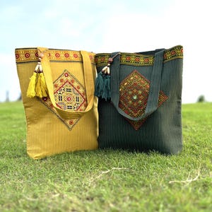 Puede incluir: Dos bolsas de tela con diseños bordados. Una bolsa es amarilla con un diseño rojo, verde y azul. La otra bolsa es verde con un diseño rojo, verde y azul.