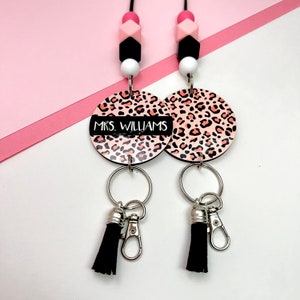 May include: A pink and black lanyard with a leopard print charm that says "MRS. WILLIAMS". The charm has a silver key ring with a black tassel attached.