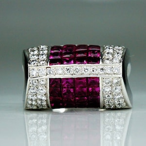 Puede incluir: Anillo rectangular de plata con un diseño simétrico. El centro presenta gemas rojas cuadradas, flanqueadas por filas de pequeñas gemas claras. Un diseño moderno y elegante con reflejos brillantes.