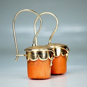 Puede incluir: Un par de pendientes de oro con colgantes de color coral. Los pendientes tienen un dise&ntilde;o delicado e intrincado y son perfectos para a&ntilde;adir un toque de elegancia a cualquier atuendo.