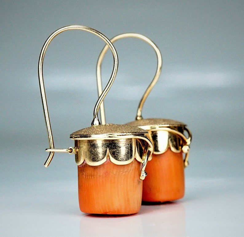 Puede incluir: Un par de pendientes de oro con colgantes de color coral. Los pendientes tienen un dise&ntilde;o delicado e intrincado y son perfectos para a&ntilde;adir un toque de elegancia a cualquier atuendo.