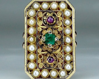 Può includere: Un anello d'oro con un designo rettangolare, che presenta uno smeraldo verde, due rubini rossi e un bordo di perle bianche.