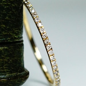 Peut inclure: Une fine bague en or, ornée d'une rangée continue de petits diamants étincelants. Le design fin de la bague et l'éclat des diamants créent une esthétique classique et élégante. La bague est présentée sur un fond doux et neutre.