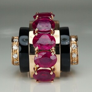 Könnte beinhalten: Ein luxuriöser Ring mit einem zentralen Band aus fünf oval geschliffenen Rubinen, gefasst in Gold. Das Design umfasst schwarze Onyx- und Diamantakzente an den Seiten, was einen auffälligen Kontrast erzeugt. Der Ring ist elegant und raffiniert.