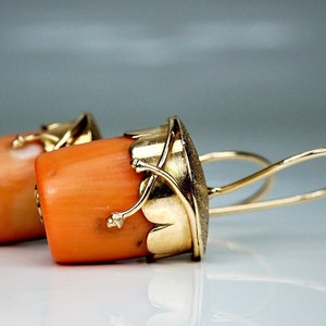 Puede incluir: Un par de pendientes de oro con piedras de coral naranja y detalles intrincados en oro. Los pendientes tienen un dise&ntilde;o colgante con un bucle de alambre.