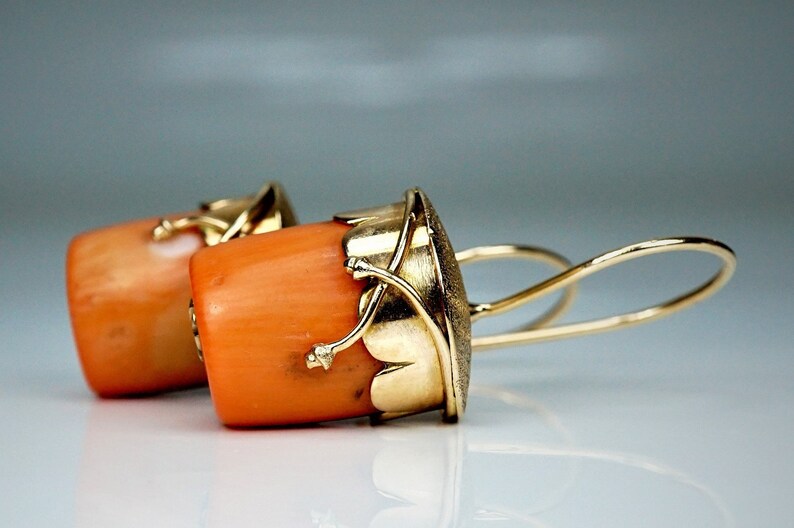 Puede incluir: Un par de pendientes de oro con piedras de coral naranja y detalles intrincados en oro. Los pendientes tienen un dise&ntilde;o colgante con un bucle de alambre.
