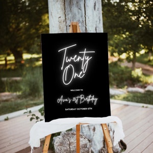 Puede incluir: Un letrero negro sobre un caballete con texto blanco que dice "Twenty One" en cursiva. Debajo, el texto dice "Welcome to Ava's 21st Birthday" y "Saturday October 15th". El letrero se exhibe al aire libre.