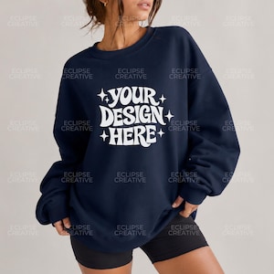 Può includere: Una felpa blu navy a girocollo con la scritta bianca YOUR DESIGN HERE in un carattere ondulato stilizzato, accentuata da icone a stella a quattro punte sui lati. Il capo presenta maniche lunghe e bordi a costine su collo, polsini e orlo.
