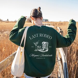 May include: Green sweatshirt with the text "Last Rodeo" and a graphic of a cocktail glass and cowboy boots. The text "Morgan's Bachelorette" and "Nashville, TN" are also printed on the sweatshirt.