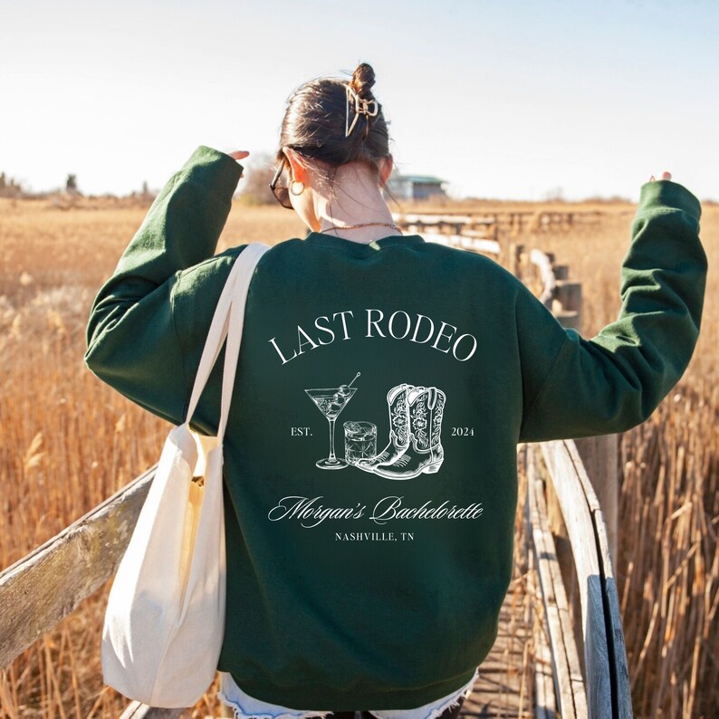 May include: Green sweatshirt with the text "Last Rodeo" and a graphic of a cocktail glass and cowboy boots. The text "Morgan's Bachelorette" and "Nashville, TN" are also printed on the sweatshirt.