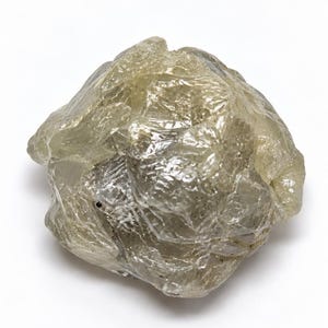 May include: A raw, uncut diamond crystal with a translucent, pale greyish-green hue. The stone features a complex, multifaceted surface with irregular, jagged edges and a natural, unpolished texture that reflects light across its uneven crystalline structure.