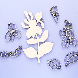 May include: A set of wooden flower cutouts in various shapes and sizes. The flowers are white and have a delicate, intricate design. The flowers are arranged on a light purple background.