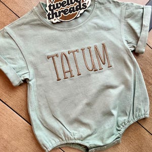 May include: A white ceramic mug with a black handle and the text "But First, Coffee" in a bold, black font. The mug is set against a blurred background, suggesting a cozy setting.