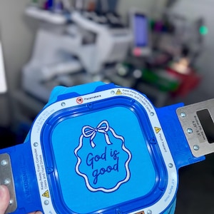May include: A blue embroidery hoop with the text "God is good" in a white and blue design. The hoop has a blue frame with silver metal accents and safety warnings. The hoop is designed for the Brother PR-Series.