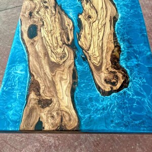 May include: Close-up of a wooden table top with a blue epoxy resin inlay. The wood has a natural grain pattern and the resin has a swirling, marbled effect.