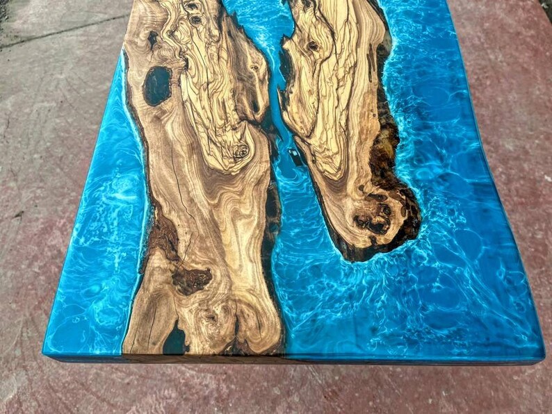 May include: Close-up of a wooden table top with a blue epoxy resin inlay. The wood has a natural grain pattern and the resin has a swirling, marbled effect.