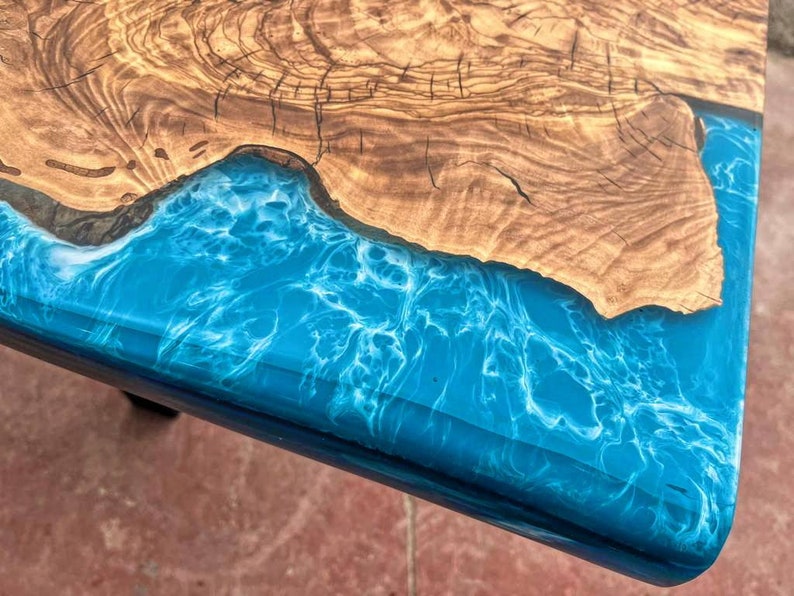 May include: Close-up of a wooden table top with a blue and white epoxy resin inlay. The resin has a swirling pattern that resembles water.