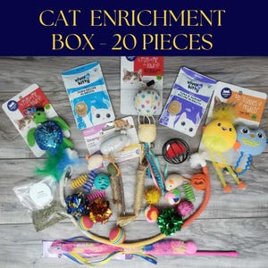 May include: A collection of cat toys and treats, including plush toys, catnip, and food pouches. The image features a variety of textures and colors, with the text "CAT ENRICHMENT BOX - 20 PIECES" at the top.