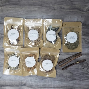 May include: An assortment of pet treats in clear pouches with white labels. The pouches contain sardines, chicken liver, cod fish, catnip, minnows, salmon bites, and beef liver. Several brown chew sticks are also visible.