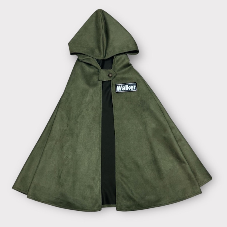 May include: An olive green hooded cape featuring a black interior lining and a single button closure at the neck. A rectangular black patch with a white border and the text "Walker" in white lettering is attached to the upper right chest area.