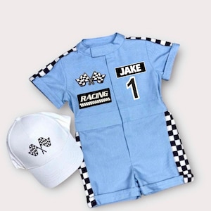May include: A light blue short-sleeve romper with black and white checkered trim along the sleeves and sides. The romper features the text JAKE, the number 1, the word RACING, and two crossed checkered flags. A matching white baseball cap is included.