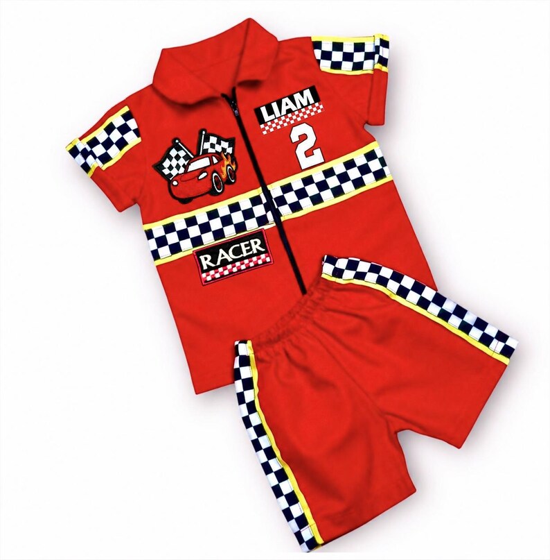May include: A red short-sleeve collared shirt with a zipper, featuring a black and white checkered pattern on the sleeves and chest. It displays a cartoon race car, the name LIAM, the number 2, and the word RACER. Matching red shorts included.